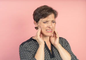 Brunette woman in her 50s in the studio with a pink background with TMJ issues